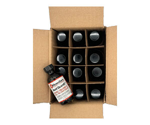 Open cardboard shipping box containing 12 small dark glass bottles with black caps arranged in a 3x4 grid; one bottle lies diagonally with a label partially visible.